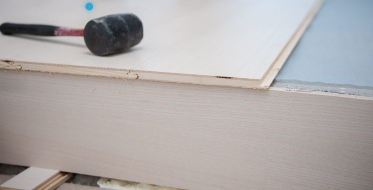 Close-up of timber floor boards being laid during an overlay installation, showing the thin board profile, tongue-and-groove edge and rubber mallet