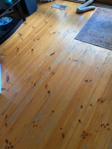Worn radiata pine floorboards with patchy coating and grey traffic wear before sanding